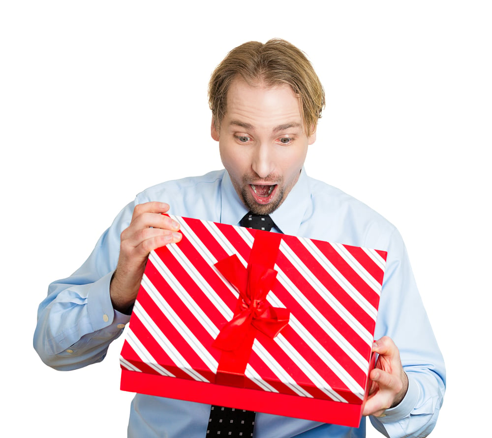 Closeup portrait of happy super excited young man about to open unwrap red gift box isolated on white background, enjoying his present. Positive human emotion facial expression feeling attitude