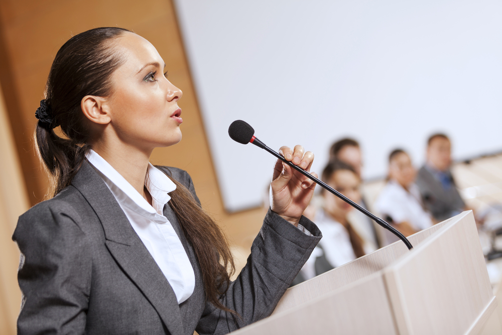 Businesswoman standing on stage and reporting for audience Businesswoman standing on stage and reporting for audience