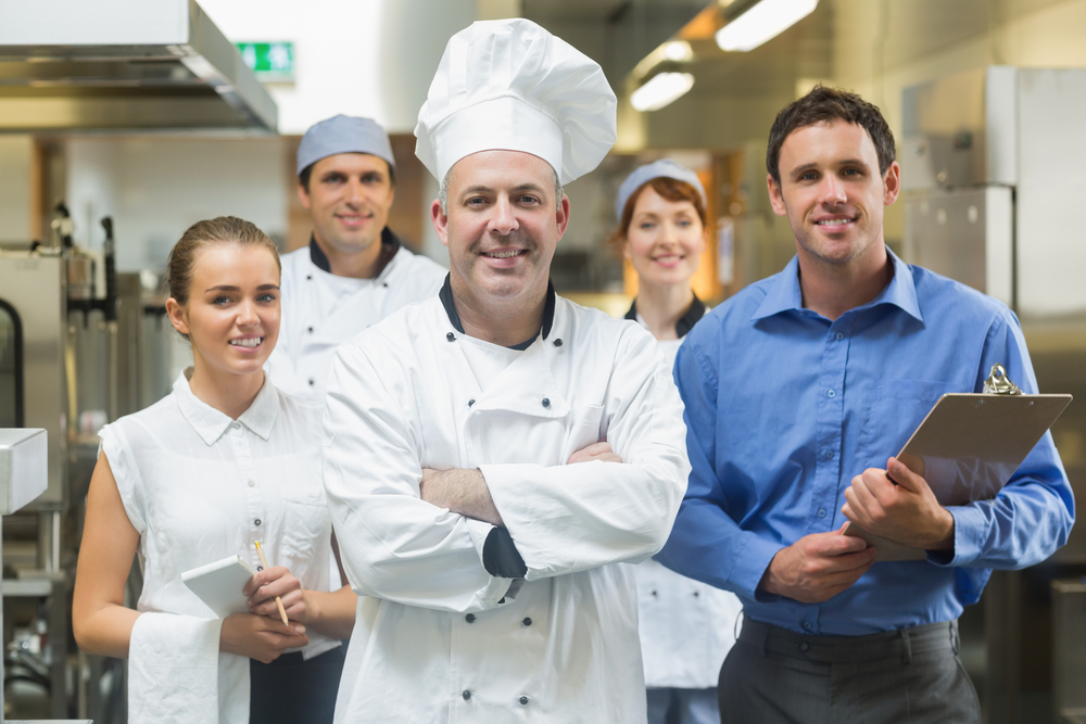 Head chef posing with the team behind him in a professional kitchen Head chef posing with the team behind him in a professional kitchen